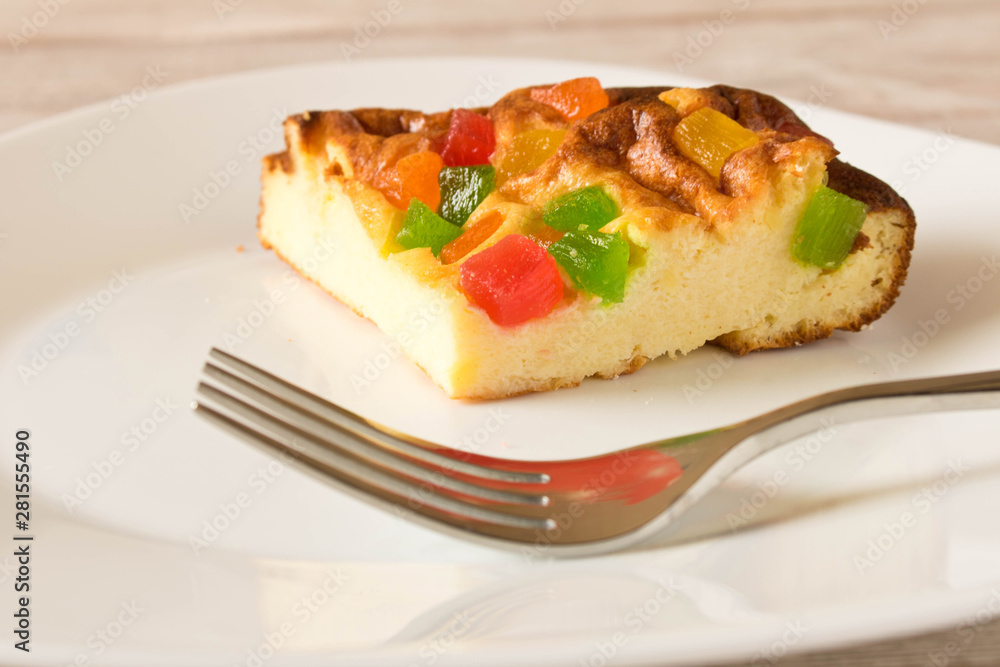 A piece of cottage cheese casserole with candied fruits on a white plate. Close up.