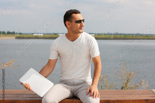 Handsome young man sitting near the sea with a laptop.