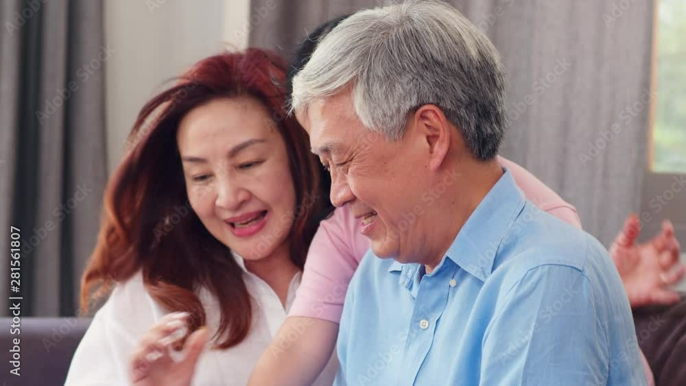 Asian grandparents and granddaughter using tablet at home. Senior Chinese, grandpa and grandma happy spend family relax with young girl check social media, lying on sofa in living room. Slow motion. Asian grandparents and granddaughter using tablet at home. Senior Chinese, grandpa and grandma happy spend family relax with young girl check social media, lying on sofa in living room. Slow motion.