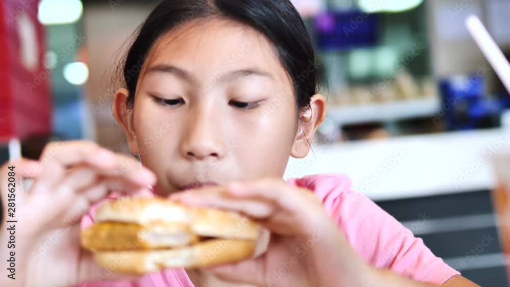 Happy Asian girl eating fish cheese burger in fastfood restaurant, lifestyle concept. Happy Asian girl eating fish cheese burger in fastfood restaurant, lifestyle concept.