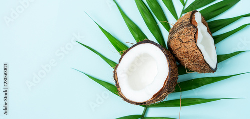 Composition with fresh halfies coconuts on palm leaves on turquoise blue light background with copy space. Exotic botanical concept for cosmetics, spa, perfume, health care products, aroma.