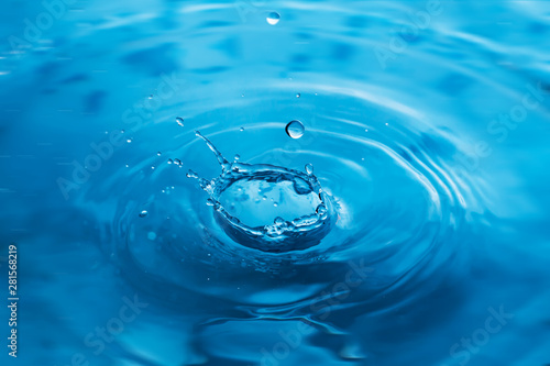 Water drops on blue surface. Water ripple background. Splashes from a drop of water. Raindrops on a blue background. The texture of the water. Aqua, turquoise, macro