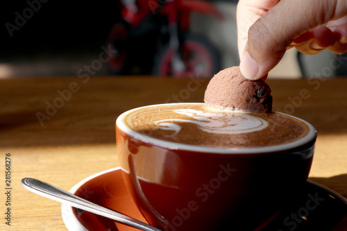 female dipping one chocolate cookie over a coffee latte