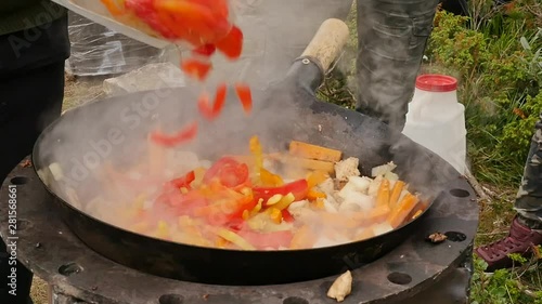 cooking vegetables with meat outdoors . fried vegetables in a cauldron. vacation concepte. smoke rises slowly over the pan. slow motion. photo