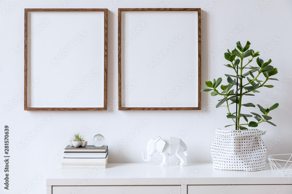 Fototapeta Stylowe wnętrze domu z dwiema brązowymi drewnianymi ramkami do zdjęć na białej półce z książkami, pięknymi roślinami, szklaną kulą i akcesoriami do domu. Minimalistyczna koncepcja wystroju białego pokoju.