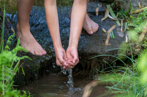 Kind schöpft frisches Quellwasser aus einem Bach als Erfrischung einer Wanderung in der grünen Natur