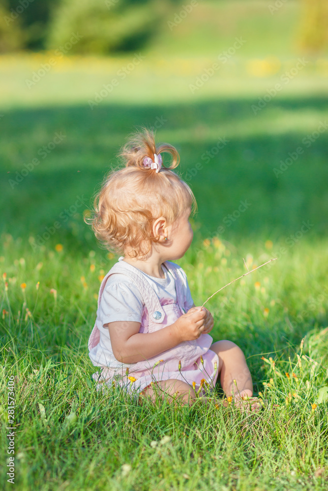 Fototapeta premium Cute little girl sits on the green grass, outdoors, summer time, blurred background
