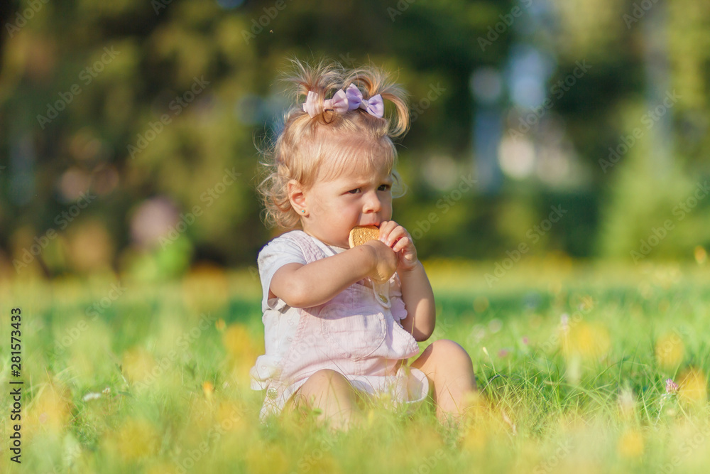 Cute little girl sits on the green grass, outdoors, summer time, blurred background Cute little girl sits on the green grass, outdoors, summer time, blurred background