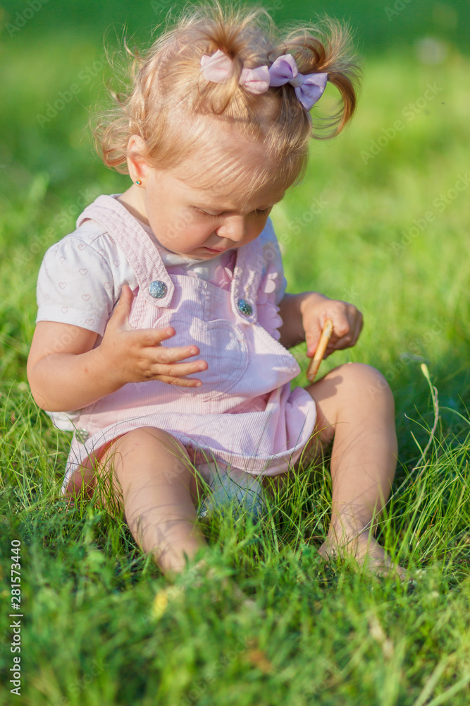 Cute little girl sits on the green grass, outdoors, summer time, blurred background Cute little girl sits on the green grass, outdoors, summer time, blurred background