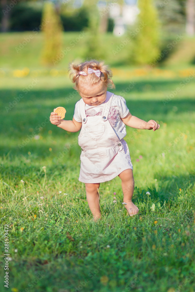 Little cute girl does her first steps with mother support, green grass, summer time, blurred background Little cute girl does her first steps with mother support, green grass, summer time, blurred background