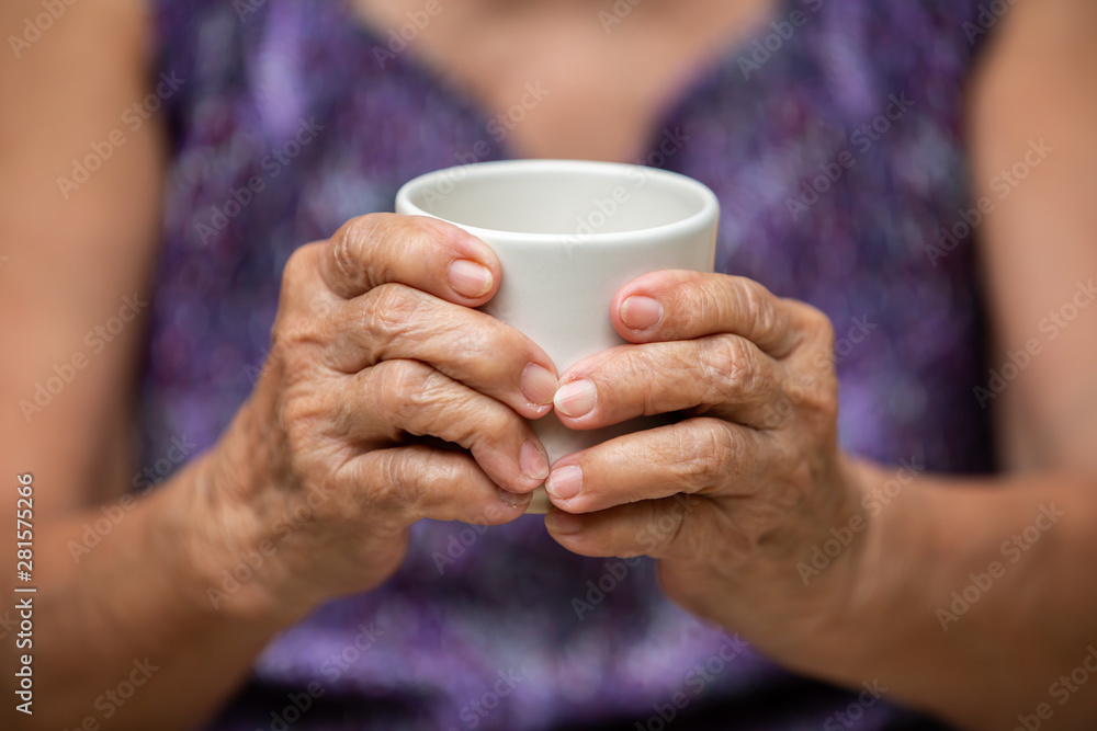 Senior woman's hands holding cup of aromatic tea in bokeh purple clothes background, Asian Body skin part, Relax time & Drink concept Senior woman's hands holding cup of aromatic tea in bokeh purple clothes background, Asian Body skin part, Relax time & Drink concept