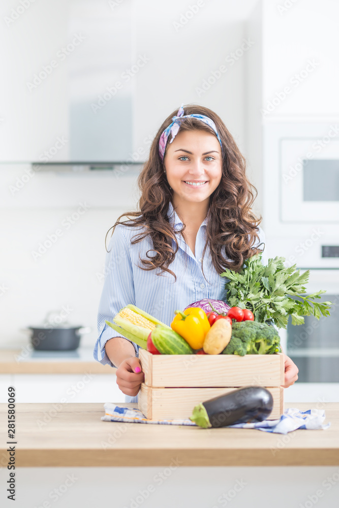 Woman in her kitchen with wooden box full of organic vegetable Woman in her kitchen with wooden box full of organic vegetable