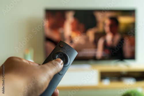 Hand holding and pressing button on television remote control, enjoying movies or home theater at home, weekend activities, lifestyles, selective focus.