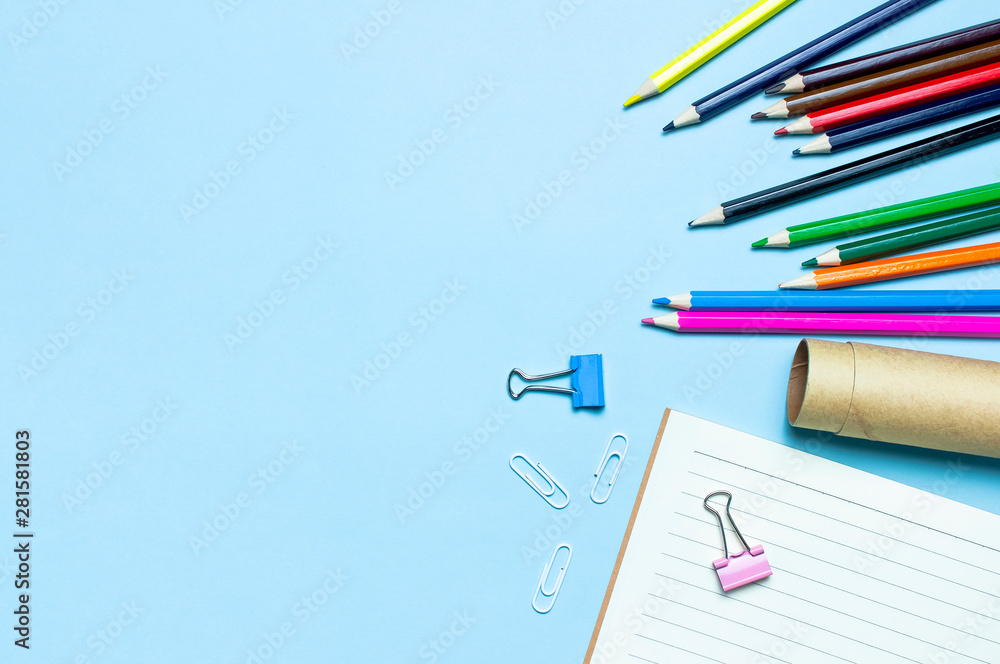 Back to school concept. Wooden colored pencils, clean school notebook in line, paper clips on blue background top view flat lay copy space. Pencils for drawing, objects for creativity Back to school concept. Wooden colored pencils, clean school notebook in line, paper clips on blue background top view flat lay copy space. Pencils for drawing, objects for creativity
