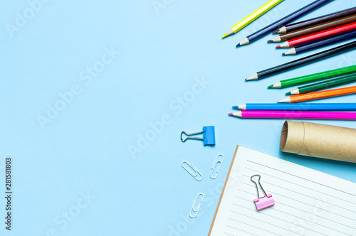 Back to school concept. Wooden colored pencils, clean school notebook in line, paper clips on blue background top view flat lay copy space. Pencils for drawing, objects for creativity