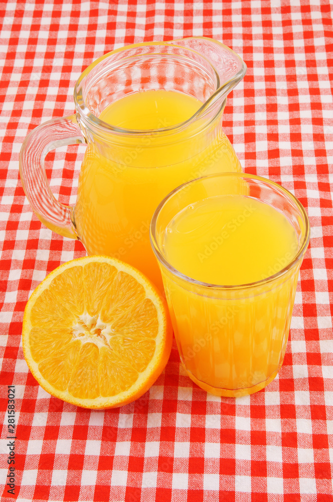 Orange juice in glass and pitcher on red tablecloth - obrazy, fototapety, plakaty 