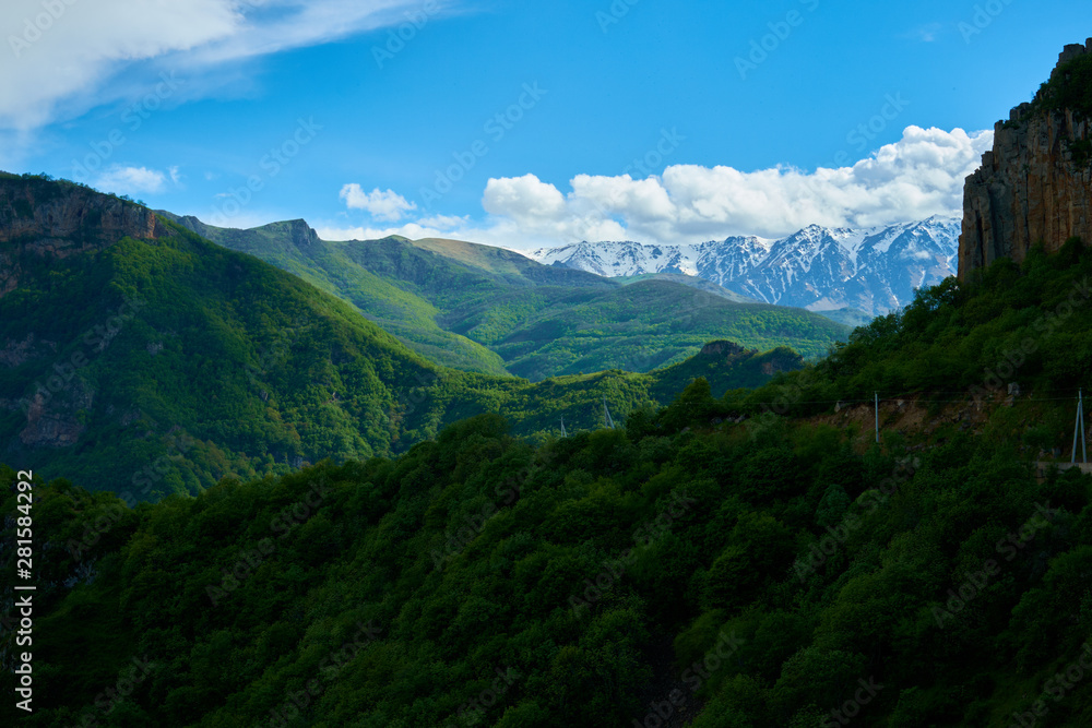 View of mountain snowy ridges on a bright sunny day with clouds in the sky. - obrazy, fototapety, plakaty 