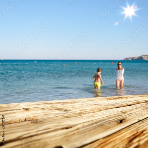 Mother and her daughter playing and having fun on the beach. Wooden table background for advertising products and decoration.