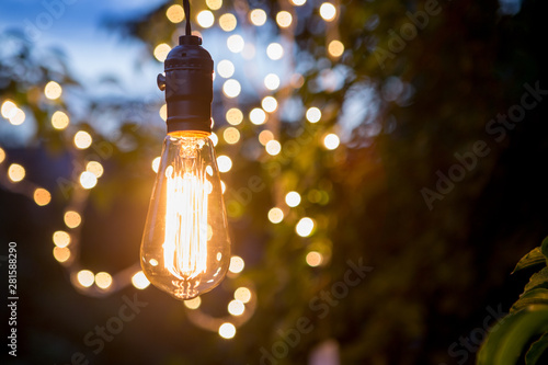 Fotografia Vintage incandescent bulb and party lights in a garden, summertime party