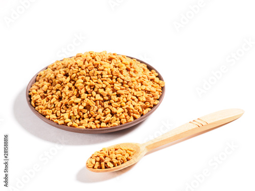 Fenugreek (Trigonella) on a clay plate and wooden spoon on a white background. Macro