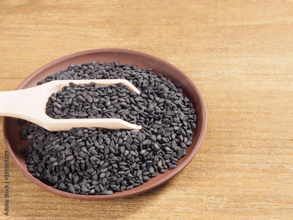 Black sesame (Sesamum indicum) in a clay plate with scoop on a wooden background Black sesame (Sesamum indicum) in a clay plate with scoop on a wooden background