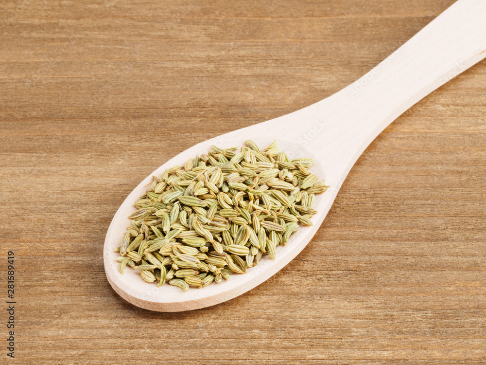 Fennel seeds (Foeniculum vulgare) in a white wooden spoon on a wooden background Fennel seeds (Foeniculum vulgare) in a white wooden spoon on a wooden background