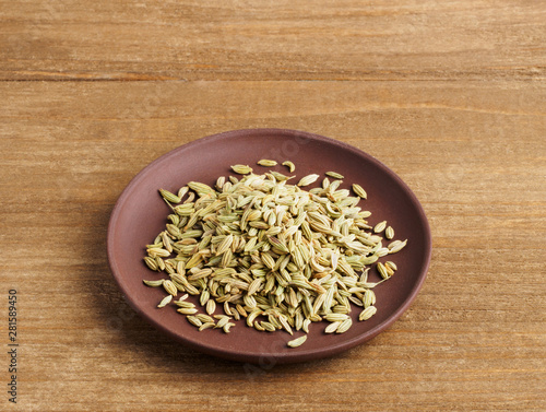 Fennel seeds (Foeniculum vulgare) in a clay plate on a wooden background