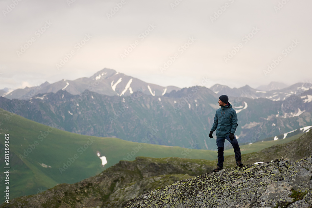 Hiker man stands against mountain top and looks away. Mountain trekking. Travel freedom concept. Copy space. Hiker man stands against mountain top and looks away. Mountain trekking. Travel freedom concept. Copy space.