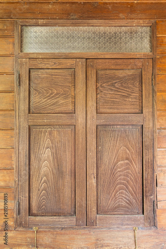 Closeup shot of closed old and vintage wooden window with pane of glass on brown hard wood panel as wall.