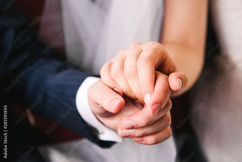 Obraz premium Bride and groom hold hands while sitting in the car. Happy marriage concept. Close up.