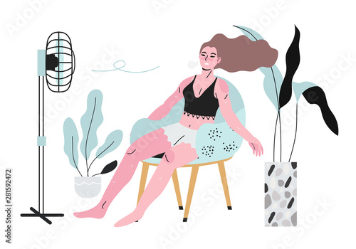 A sweaty girl or a woman sitting in an arm chair in front of a fan during hot summer days and not feeling well because of the terrible heat.