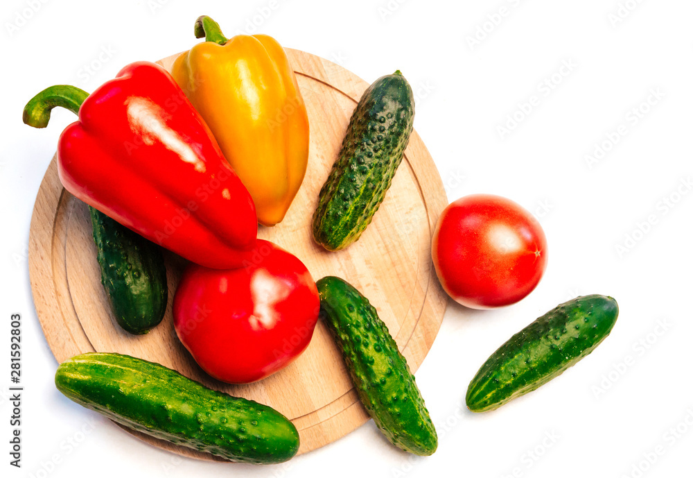cucumbers, peppers and tomatoes on a wooden cutting board on a white background. vegetables on a round cutting board cucumbers, peppers and tomatoes on a wooden cutting board on a white background. vegetables on a round cutting board