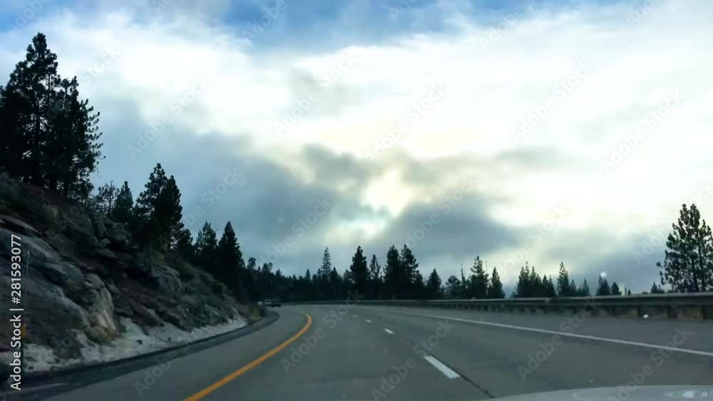 Dramatic Time lapse shot of a car as it travels down a country highway through snowy mountains, Pine trees clouds, other vehicles can been seen in the adjoining lanes. Driving from Lake Tahoe Dramatic Time lapse shot of a car as it travels down a country highway through snowy mountains, Pine trees clouds, other vehicles can been seen in the adjoining lanes. Driving from Lake Tahoe