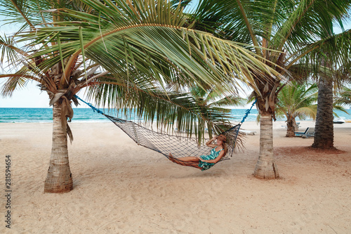 Woman relaxing in the hammock on tropical beach, hot sunny day. Young womansitting in a hammock between palm trees. Vacation in Sri Lanka photo