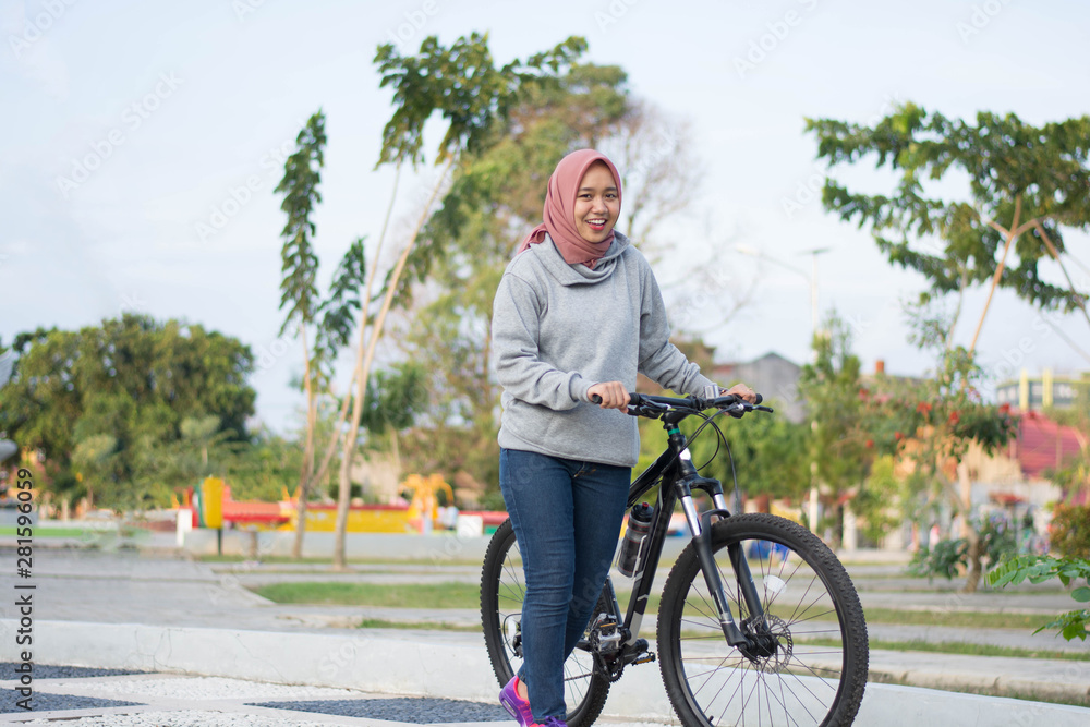 portrait of hijab woman posing next to a bicycle and pushing her bicycle in front of the camera portrait of hijab woman posing next to a bicycle and pushing her bicycle in front of the camera
