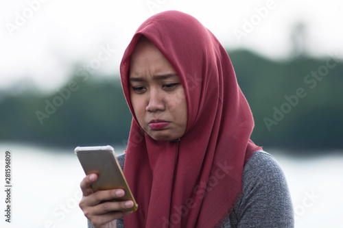close up shot of hijab woman sitting by holding the cellphone sad and angry
