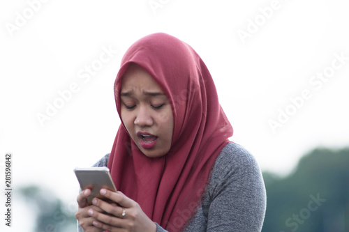 close up shot of hijab woman sitting by holding the cellphone sad and angry