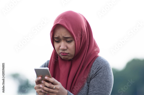 close up shot of hijab woman sitting by holding the cellphone sad and angry