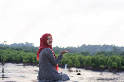portrait of hijab woman was sitting on the boardwalk in the beautiful sunshine of the mangrove park and taking a photo facing the camera