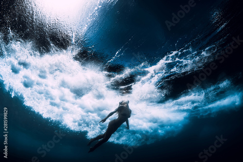Woman dive underwater with big ocean wave.