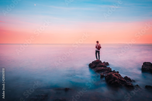 young man stand on a rock in the foreground of him have the sea and sky brightly colored look like a dream in heaven.