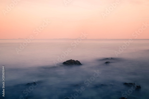 Long exposure of the waves that cover the rocks in the sea and the beautiful colors of the sky in dusk looks like a dream. © phungatanee