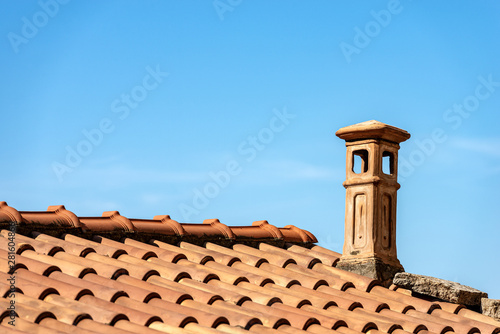 Closeup of a house roof with a terracotta tiles and chimney on a clear blue sky. Liguria, Italy, Europe