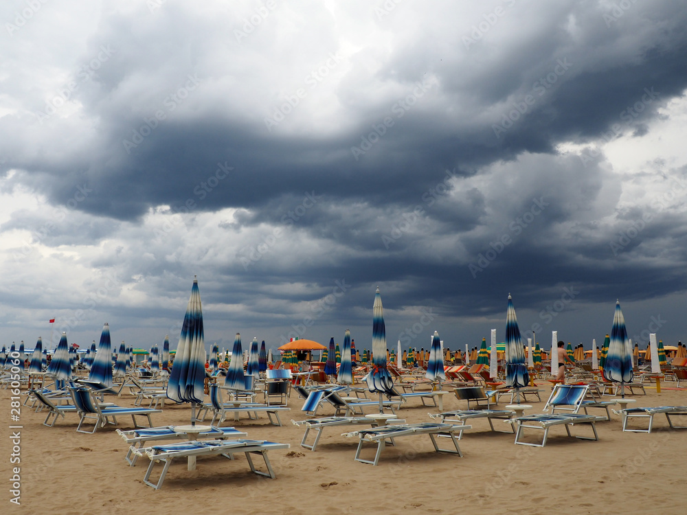 Sea, beach and closed sunshades approaching thunderstorms
