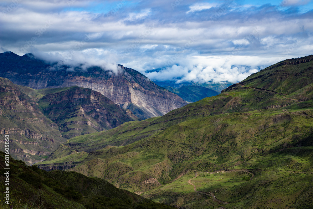 Mountain landscape beautiful green mountains with Alpine lush meadows cloudy sky background.