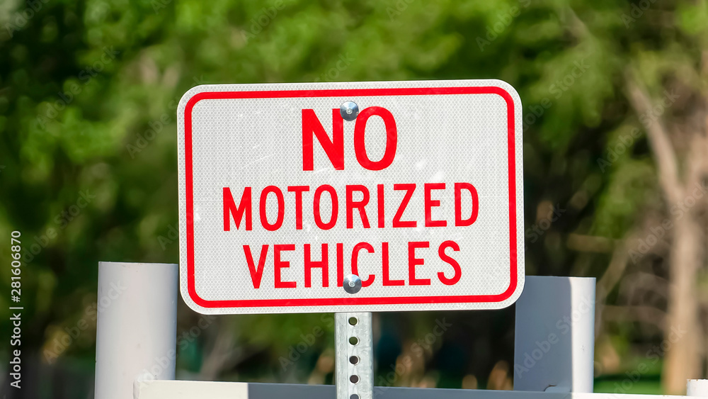 Panorama Close up view of a No Motorized Vehicle sign against a road with a white gate
