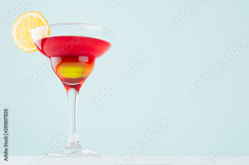 Bright summer beverage margarita for party with red and yellow liquor, orange slice on white wood board and mint color wall.