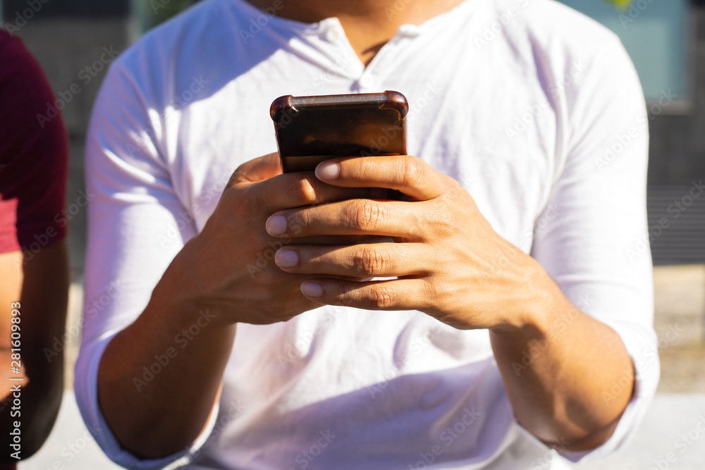 Man in white casual shirt standing outside and using smartphone. Closeup male hands holding mobile phone. Mobile phone using concept Man in white casual shirt standing outside and using smartphone. Closeup male hands holding mobile phone. Mobile phone using concept
