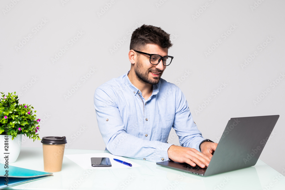 Happy young man, wearing glasses and smiling works on his laptop to get all his business done early in the morning with his cup of coffee Happy young man, wearing glasses and smiling works on his laptop to get all his business done early in the morning with his cup of coffee