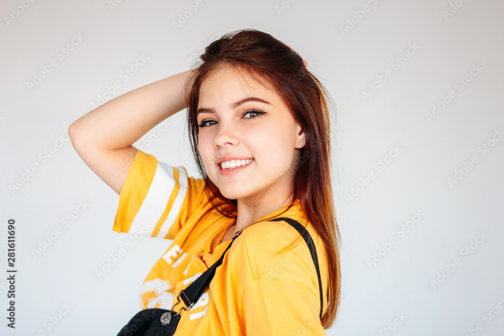 Portrait of happy carefree smiling teenager girl with dark long hair in yellow t-shirt on grey background Portrait of happy carefree smiling teenager girl with dark long hair in yellow t-shirt on grey background